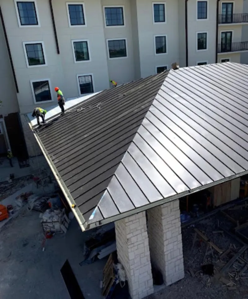 Crew installing standing seam metal roof panels on a commercial project in Pell City